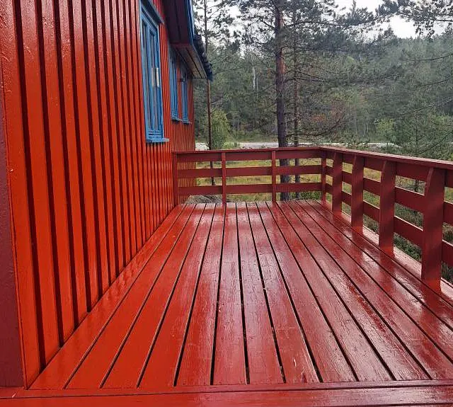 Rødmalt terrasse med rekkverk og blå vindusrammer